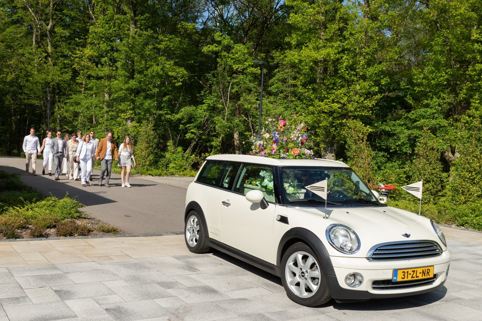Familie loopt achter de Minirouwauto, met een groot bloemstuk op het dak